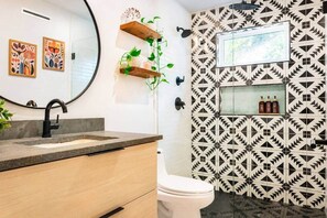 A bathroom with a modern design, featuring a sink with a curved faucet, a toilet, and a shower area. There are decorative plants on floating shelves and a patterned wall. - Mid-Century Tiny House (Austin)