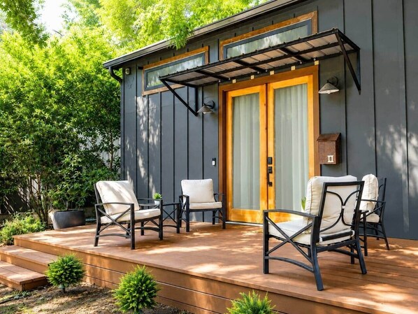 A modern outdoor seating area with a wooden deck, two chairs, and a small table. - Mid-Century Tiny House (Austin)