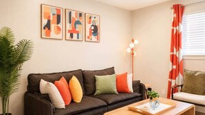 A living room with a dark brown sofa, colorful cushions, a wooden coffee table, and abstract wall art. - Retro Oasis (Austin)