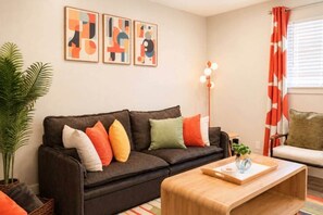 Ein Wohnzimmer mit einem dunkelbraunen Sofa, bunten Kissen, einem Holztisch und abstrakter Wandkunst.