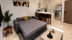 A compact living space with a bed, a small dining table, a kitchen area, and a potted plant. - Jungle Guardian Beach Club Stays & Tours (Tulum)