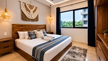 Un dormitorio moderno con cabecera de madera, una cama grande con muchos almohadones, vistas a la vegetación por la ventana y un ventilador de techo.
