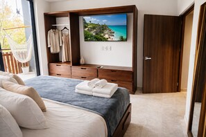 Un dormitorio con cama, cómoda de madera, televisor y vista a la playa.