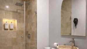 Un bany modern amb plat de dutxa envoltat de vidre, vàter, piques rodones sobre un moble i un mirall gran.