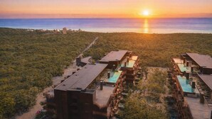 Un complex turístic amb diversos edificis, piscines exteriors i vista a l'oceà al capvespre.