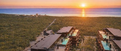 A resort with multiple buildings, outdoor pools, and a view of the ocean at sunset.
