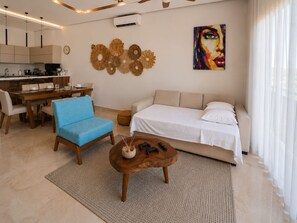 Un salon moderne avec un canapé, un fauteuil bleu, une table basse et un tableau accroché au mur.