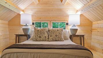Un dormitorio acogedor con techo de madera, una cama con almohadas estampadas y dos lámparas de noche.