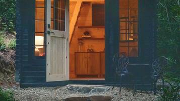 A wooden cabin with a door open, revealing a kitchen area with cabinets and a sink.