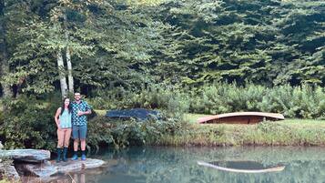 A natural setting with a body of water, a wooden bridge, and dense foliage.