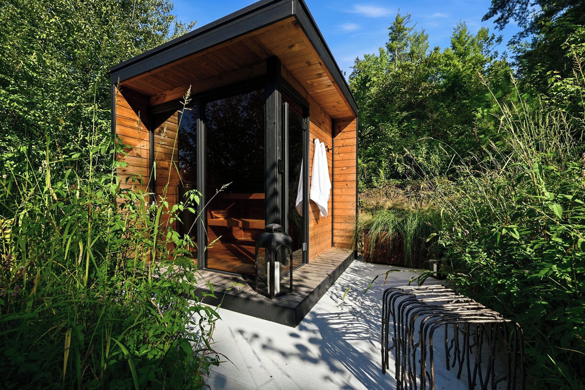 A wooden cabin with a glass door, surrounded by dense greenery.