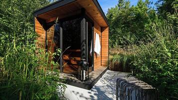 A wooden cabin with a glass door, surrounded by dense greenery.