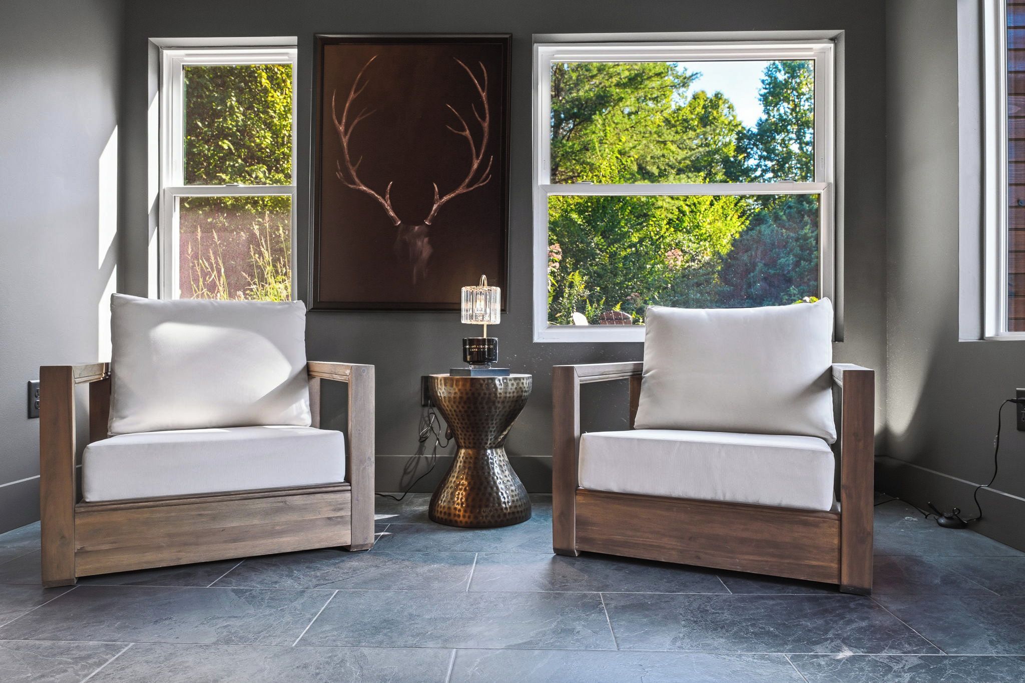 Una habitación con dos sillones, una mesita auxiliar y un ventanal con vistas a árboles.