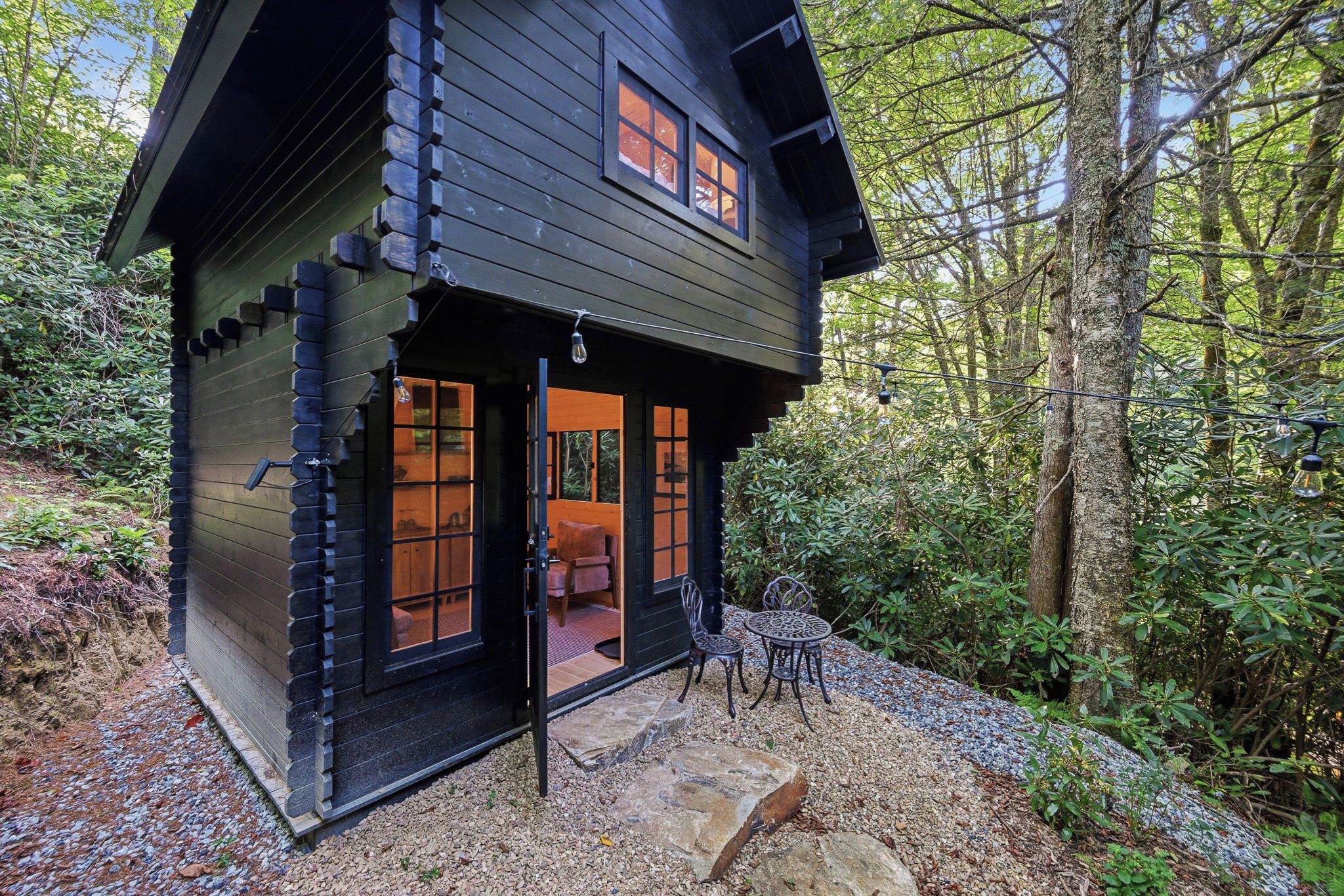A cabin with a wooden exterior, a front door, and a small patio area with outdoor seating.