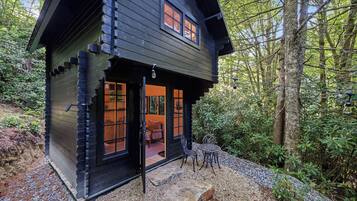 A cabin with a wooden exterior, a front door, and a small patio area with outdoor seating.