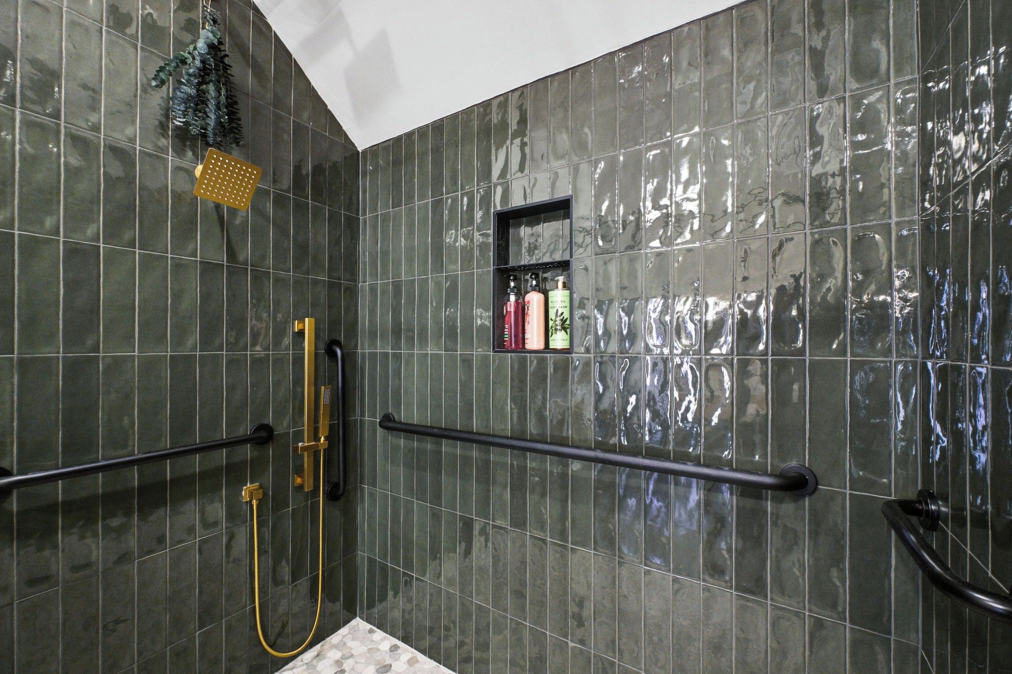 Un baño con ducha, barra de apoyo y estante con artículos de aseo.