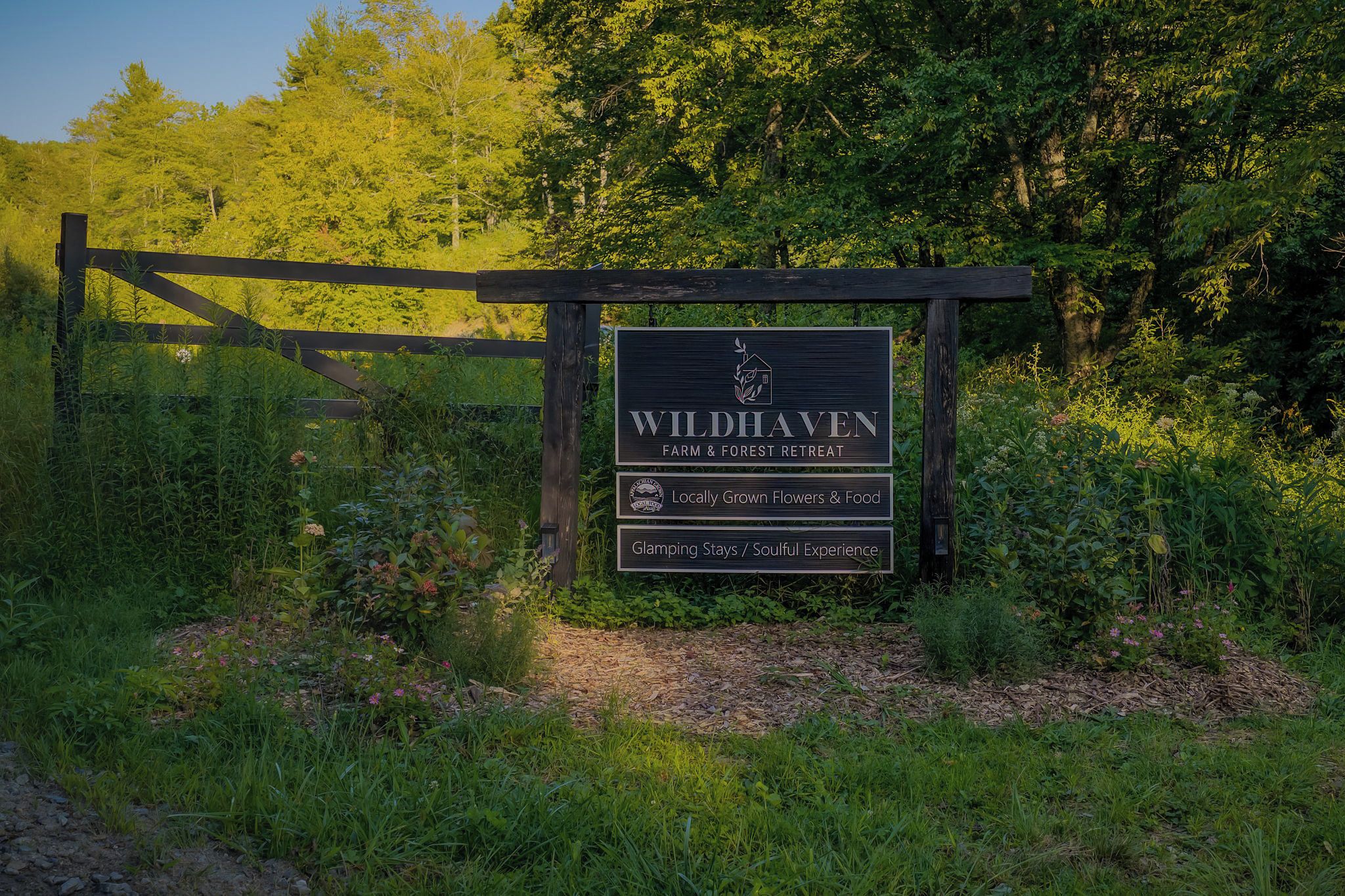 Señal de Wildhaven Farm & Forest Retreat, destacando flores y comida de producción local, estancias de glamping y una experiencia enriquecedora.