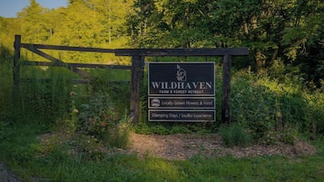 Señal de Wildhaven Farm & Forest Retreat, destacando flores y comida de producción local, estancias de glamping y una experiencia enriquecedora.