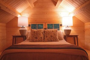 Un dormitorio acogedor en una cabaña de madera con una cama, dos mesitas de noche y dos lámparas.