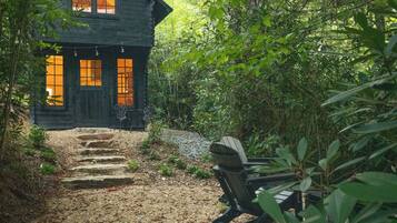 A wooden cabin with a stone staircase leading to a door with windows, surrounded by dense foliage.
