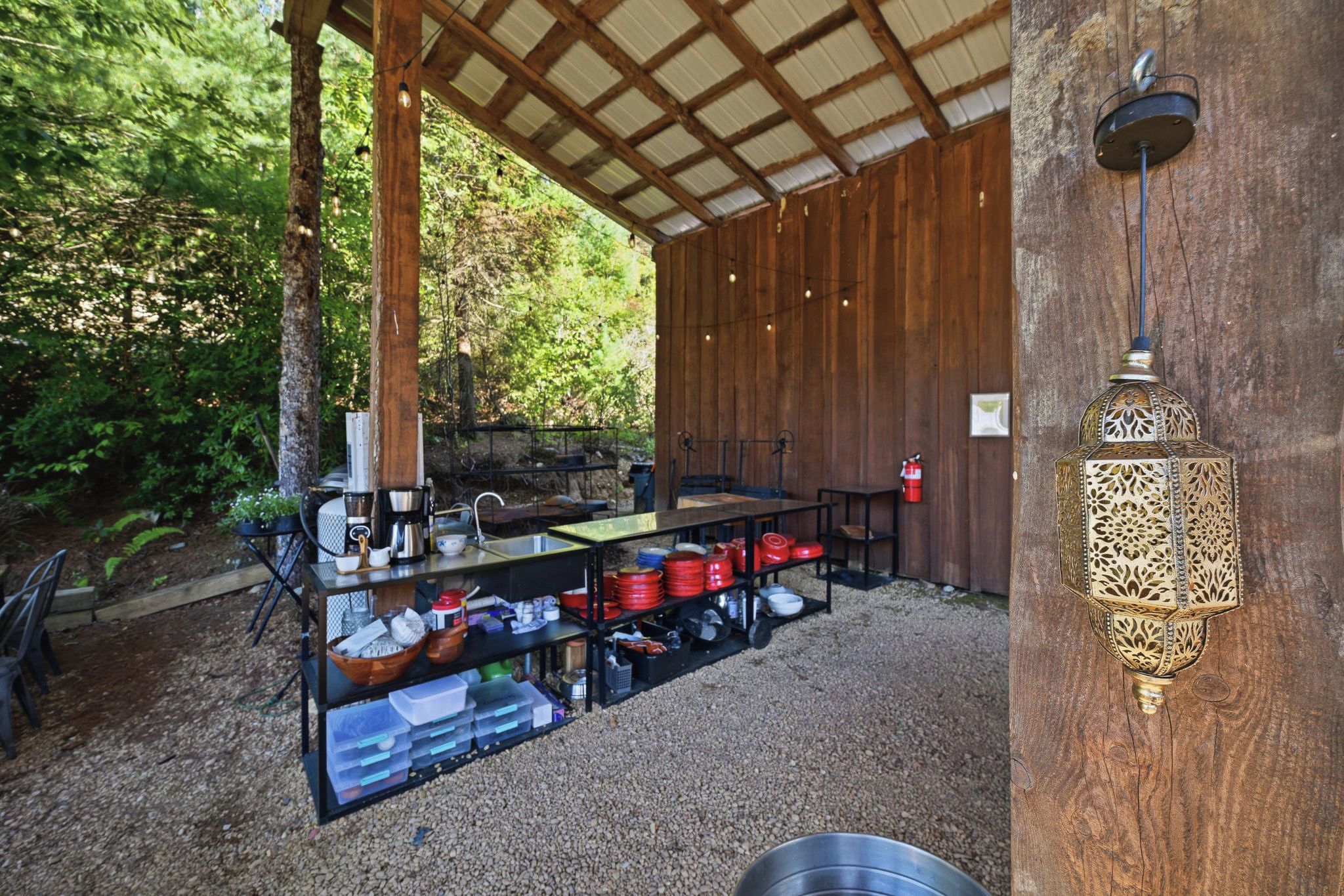 An outdoor kitchen area with a metal table, shelves with kitchenware, and a decorative lantern.