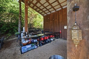 Un área de cocina al aire libre con una mesa de metal, estantes con utensilios de cocina y un farol decorativo.