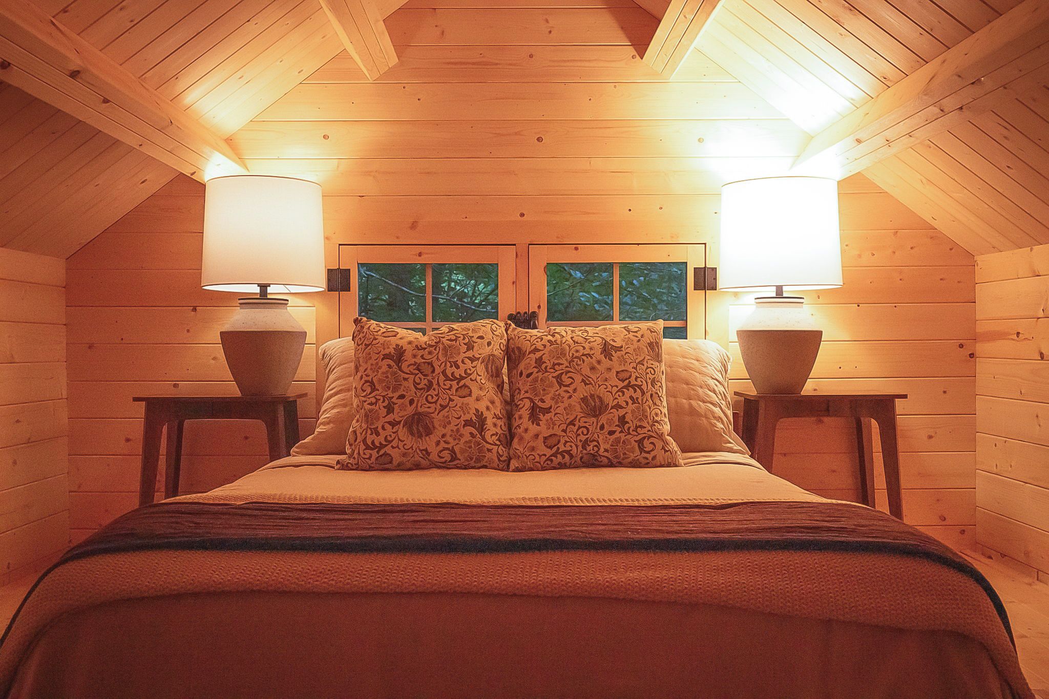 A cozy bedroom with a wooden ceiling, a bed with patterned pillows, and two bedside lamps.
