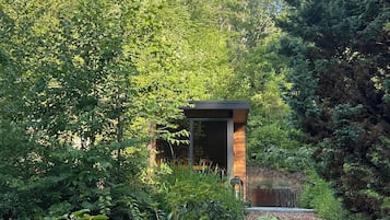 A small wooden cabin surrounded by dense greenery and trees.
