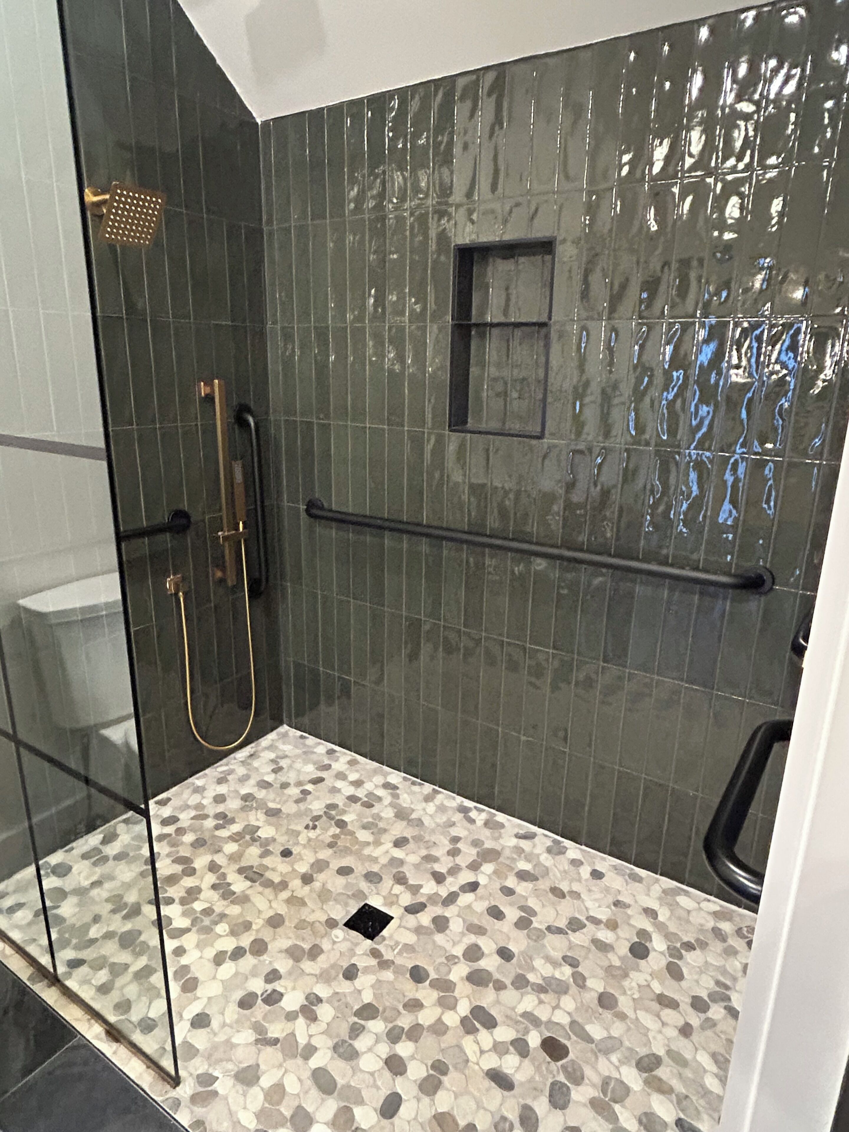 A shower with a glass door, a handrail, and a pebble-patterned floor.