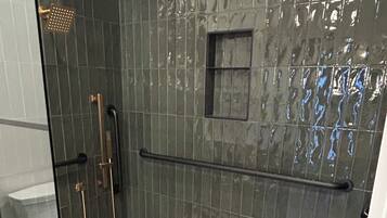 A shower with a glass door, a handrail, and a pebble-patterned floor.