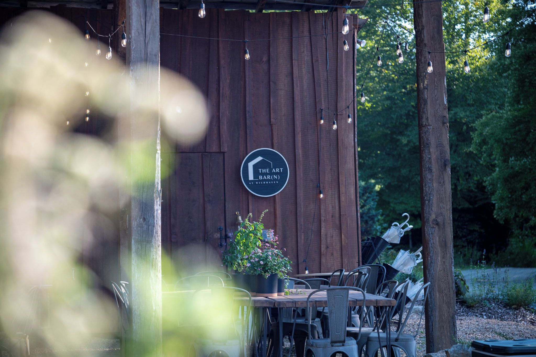 A rustic wooden structure with a sign for 'The Art Bar (N) at Wildhaven' and outdoor seating with chairs and umbrellas.