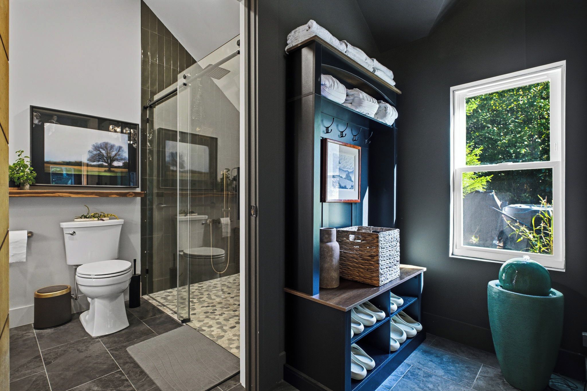 Un baño moderno con cabina de ducha de vidrio, inodoro y estante empotrado con toallas y objetos decorativos.