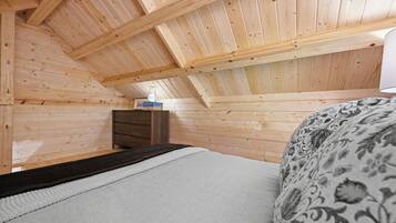 Un interior de madera con techo inclinado, una cama con cubierta estampada y un aparador.