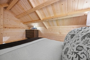 A wooden interior with a sloped ceiling, a bed with a patterned cover, and a dresser.