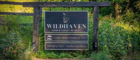 A sign for Wildhaven Farm & Forest Retreat with a logo, indicating locally grown flowers & food, and mentions glamping stays and a soulful experience.