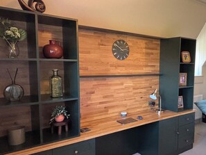 A room with a wooden wall, a clock, shelves with various items, and a desk with a lamp and a mouse.