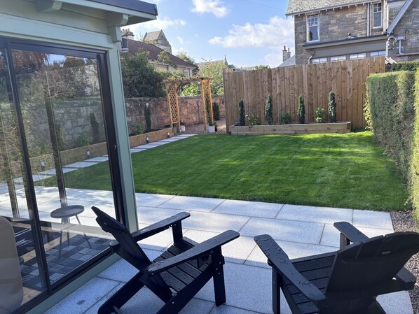 A patio area with a glass door leading to a garden, a wooden fence, and outdoor seating.