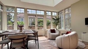 Une pièce spacieuse avec un plafond haut, de grandes fenêtres, un coin repas et un espace salon équipé d’un téléviseur.