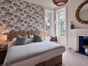 Ein Schlafzimmer mit einem großen Bett, einem Kamin und einem Fenster mit Blick auf Grünflächen.