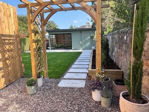 A wooden pergola structure, a gravel pathway, and potted plants in a garden setting.