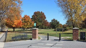 A paved entrance to a park with a brick pillar, a metal fence, and a sign indicating the name of the park. - Modern 1-Bedroom Apartment with AC in Flushing (FLUSHING)