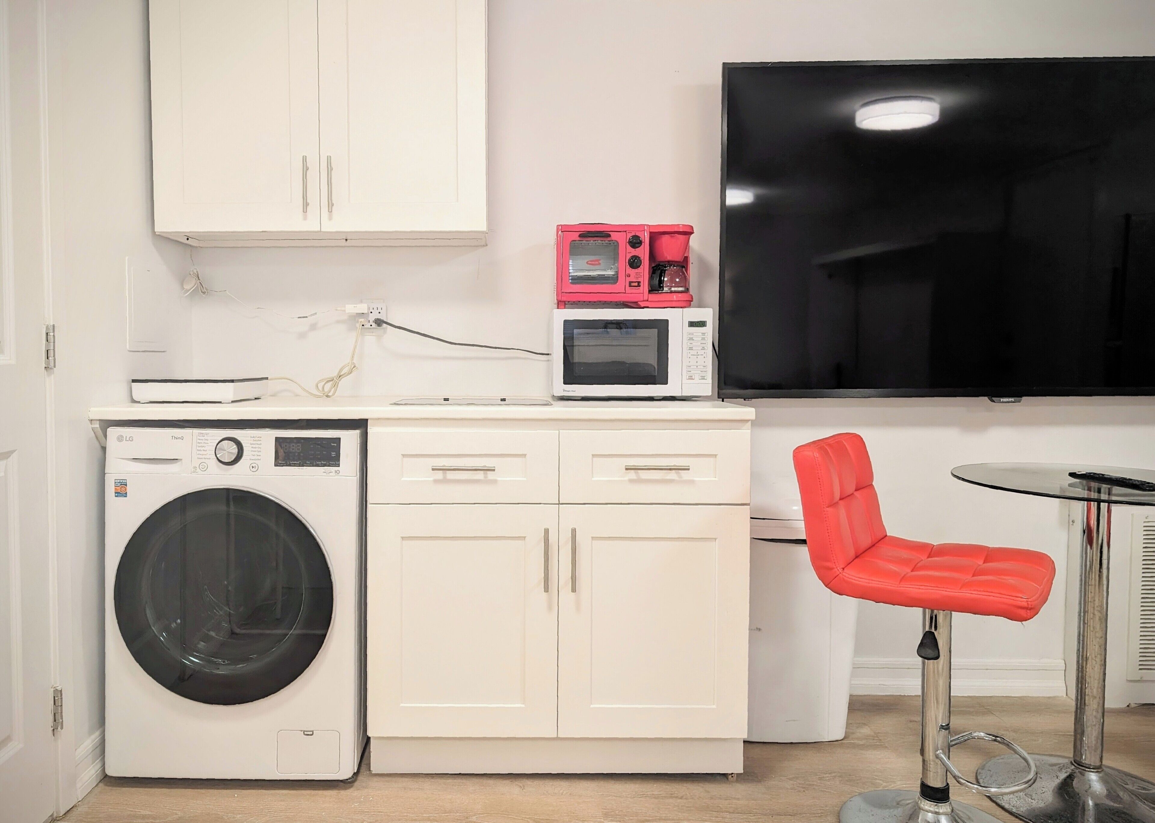 A compact kitchenette with a washing machine, microwave, and a flat-screen TV.