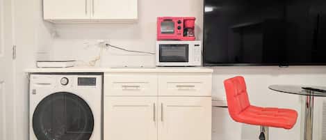 Cocina americana compacta con lavadora, microondas y televisor de pantalla plana.