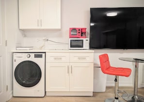 A compact kitchenette with a washing machine, microwave, and a flat-screen TV. - Brand New Studio! Washer/Dryer! Parking! Main St! (FLUSHING)