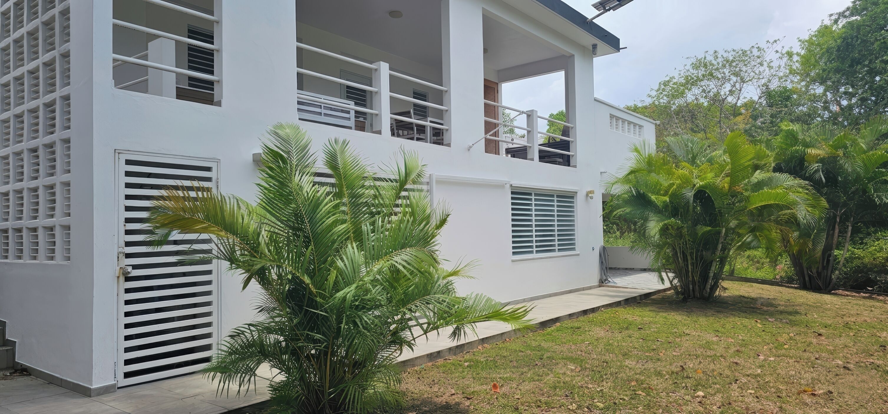 A modern two-story building with a balcony, large windows, and a well-maintained lawn with palm trees.