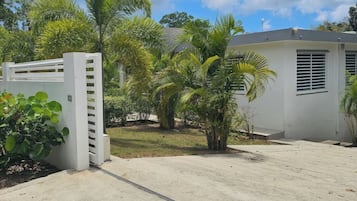 A gated entrance with a concrete pathway leading to a building with a white exterior and a window with horizontal blinds.