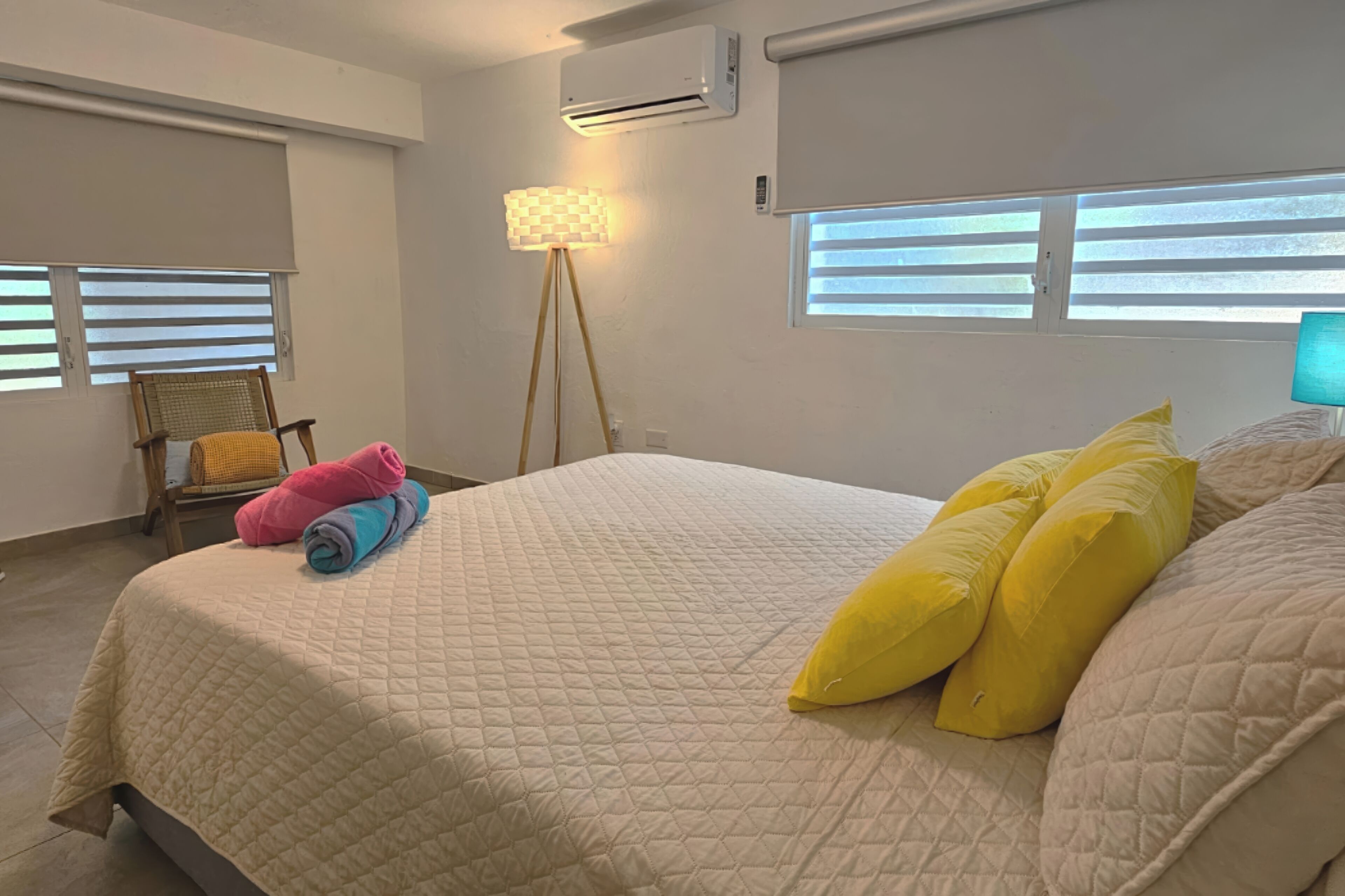 Un dormitorio con una cama, una silla, una lámpara y aire acondicionado.