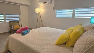 Un dormitorio con una cama, una silla, una lámpara y aire acondicionado.