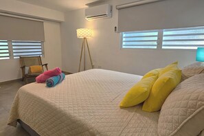Un dormitorio con una cama, una silla, una lámpara y aire acondicionado.