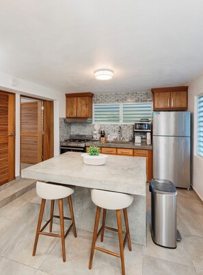 Cocina moderna con isla central, armarios de madera, refrigerador de acero inoxidable y un cubo de basura.